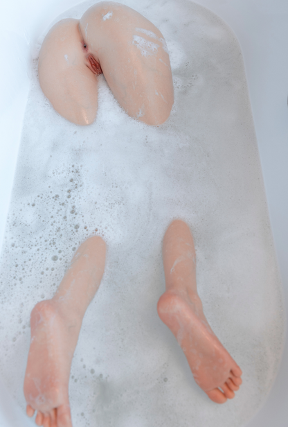 Realistic female body part with detailed texture floating in bubbly bathwater, showcasing lifelike skin tone and form.