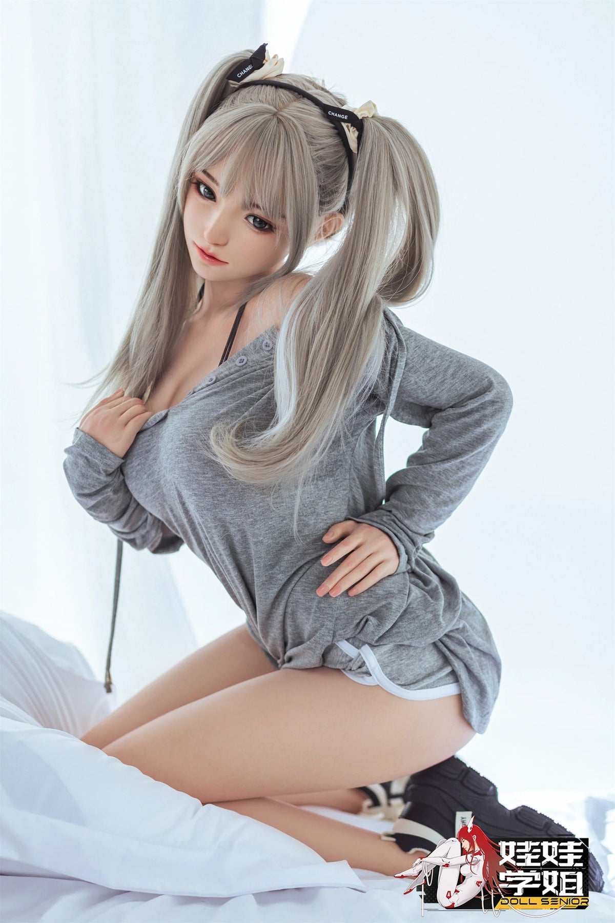Realistic female doll with silver twin tails, gray loungewear, and soft skin texture posing on white bedding