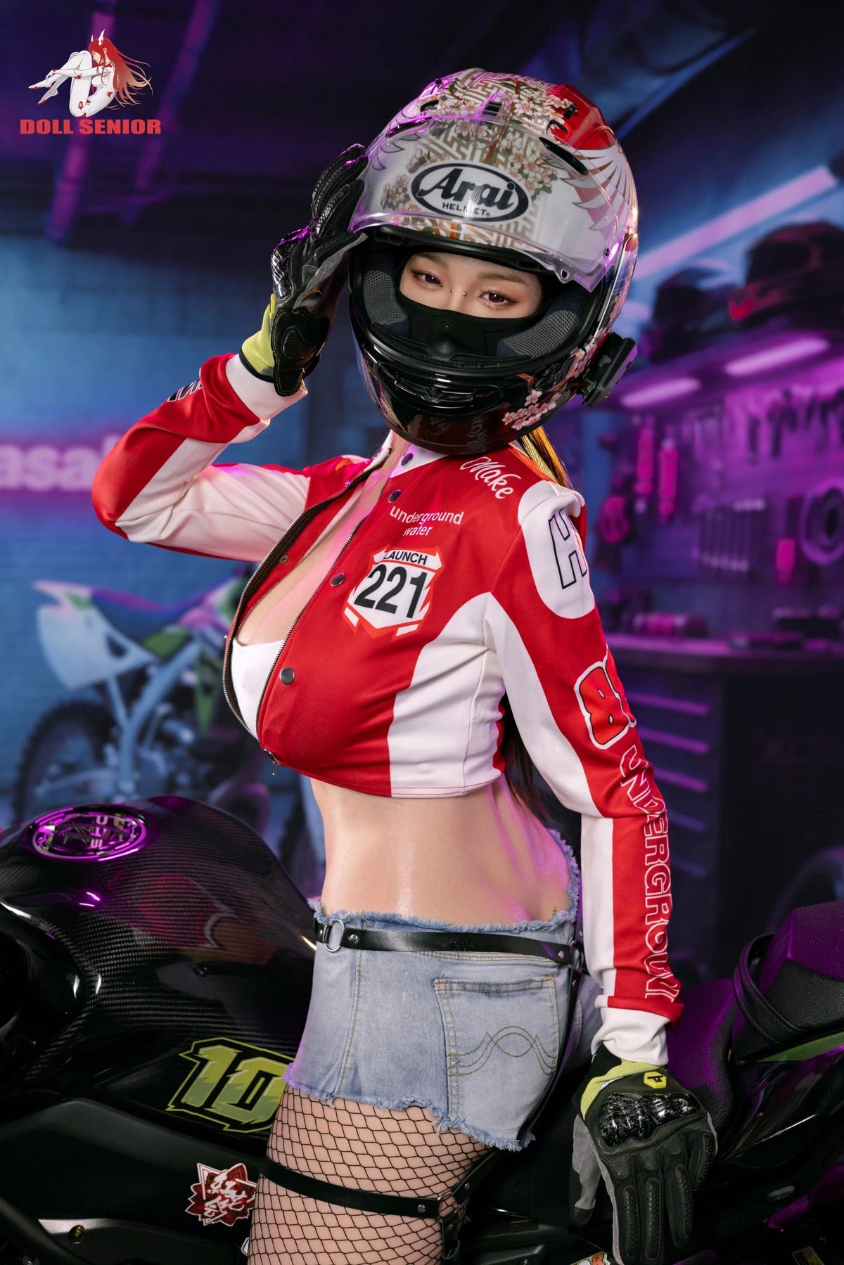 Realistic female doll in red racing jacket, floral helmet, and denim shorts posing beside motorcycle