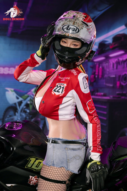 Realistic female doll in red racing jacket, floral helmet, and denim shorts posing beside motorcycle